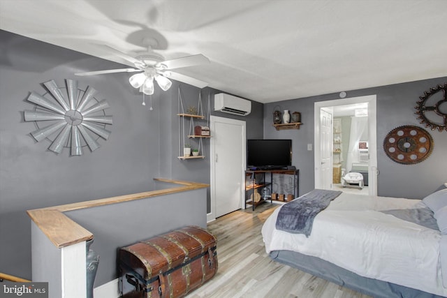 bedroom featuring a ceiling fan, ensuite bathroom, a wall unit AC, and wood finished floors