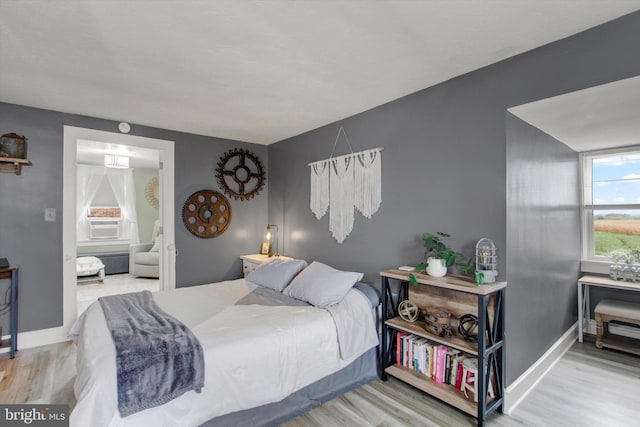 bedroom featuring cooling unit, ensuite bath, baseboards, and wood finished floors