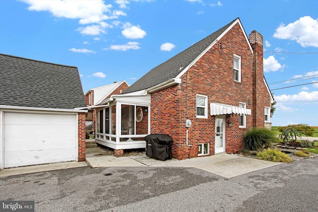 view of side of property with brick siding, a shingled roof, a chimney, a garage, and a sunroom