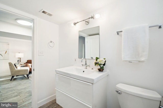 ensuite bathroom featuring visible vents, toilet, wood finished floors, baseboards, and vanity