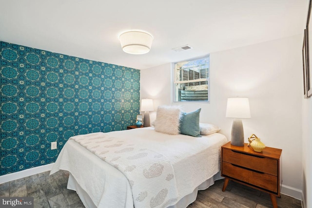 bedroom with an accent wall, wood finished floors, visible vents, and baseboards