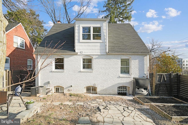 rear view of property featuring fence, roof with shingles, a garden, a chimney, and brick siding