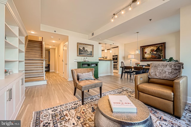 living area featuring light wood finished floors, visible vents, baseboards, stairs, and rail lighting