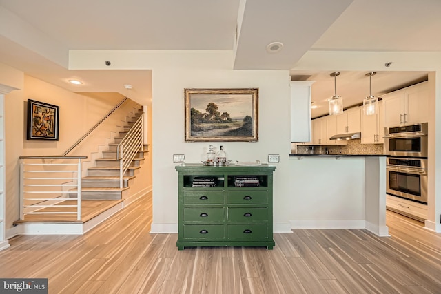 interior space featuring light wood finished floors, dark countertops, under cabinet range hood, stainless steel double oven, and white cabinetry