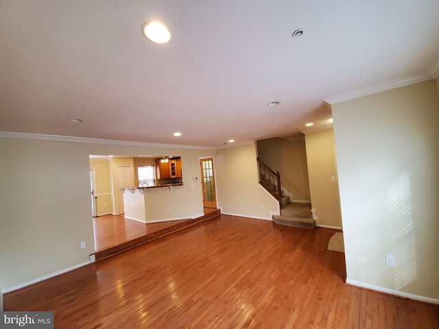 unfurnished living room with hardwood / wood-style floors, crown molding, stairs, and baseboards