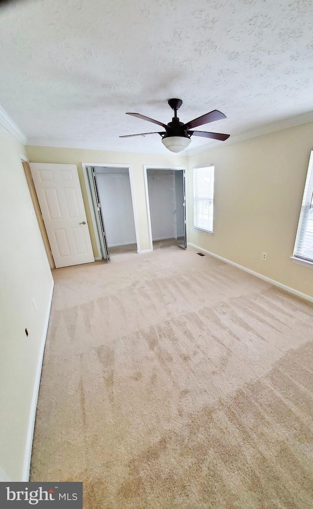 unfurnished bedroom featuring carpet flooring, baseboards, two closets, and a textured ceiling