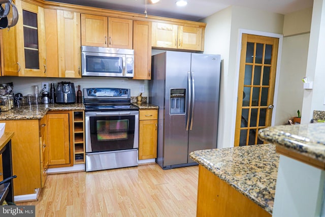 kitchen featuring light stone counters, glass insert cabinets, appliances with stainless steel finishes, and light wood-style flooring