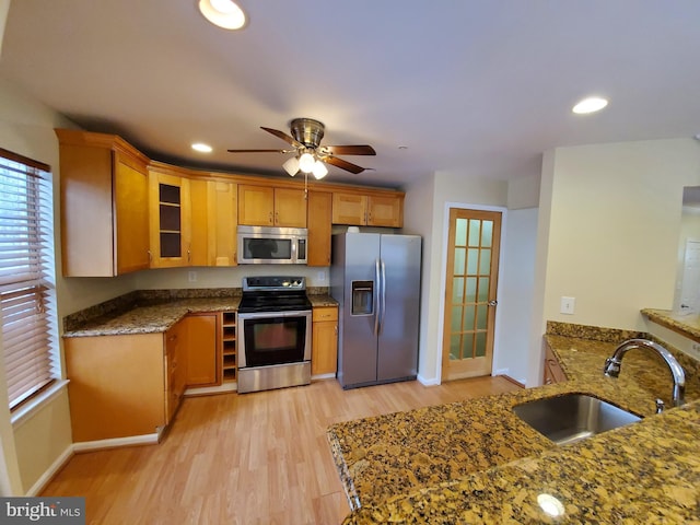 kitchen featuring dark stone countertops, light wood finished floors, a sink, stainless steel appliances, and glass insert cabinets