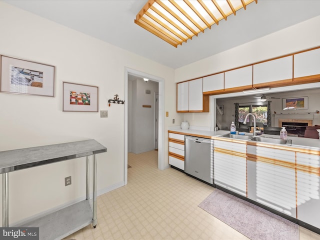 kitchen featuring a fireplace, a sink, light countertops, white cabinets, and stainless steel dishwasher