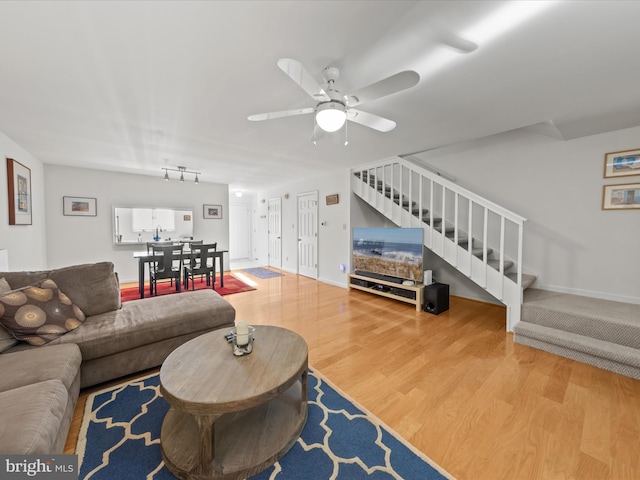 living area with a ceiling fan, stairs, baseboards, and wood finished floors