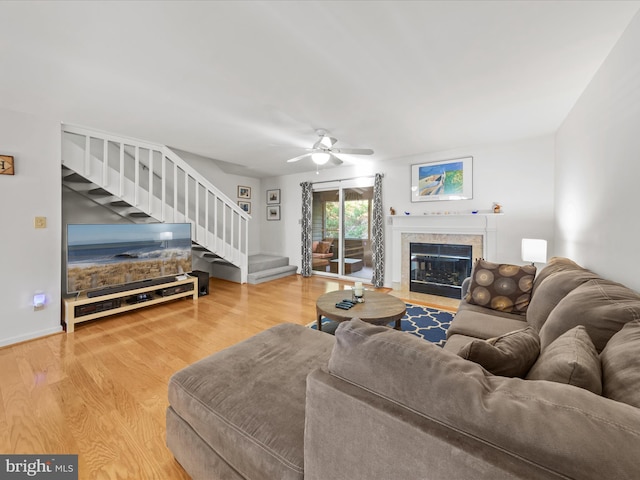 living area featuring stairway, a fireplace with flush hearth, wood finished floors, and a ceiling fan