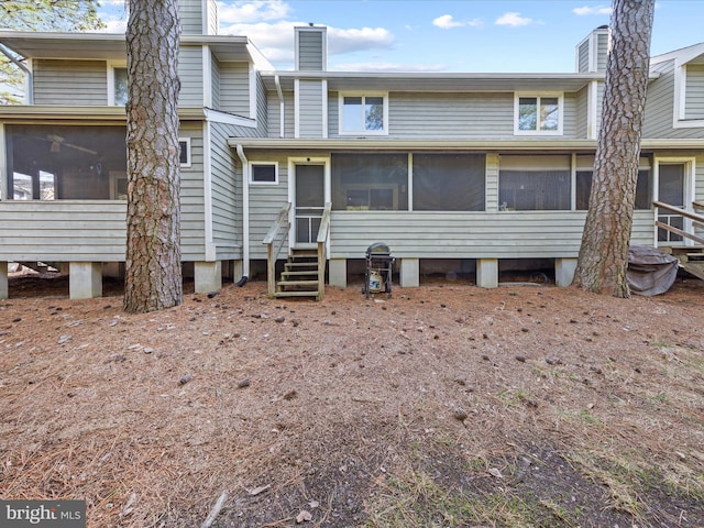 back of property with entry steps, a sunroom, and a chimney