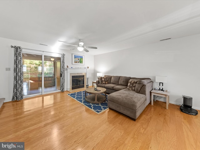 living area featuring visible vents, baseboards, ceiling fan, a tile fireplace, and wood finished floors