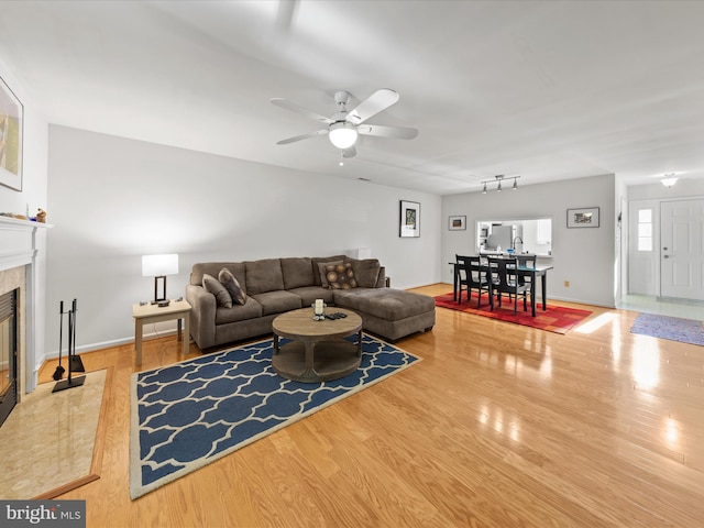 living area with a fireplace, baseboards, a ceiling fan, and wood finished floors