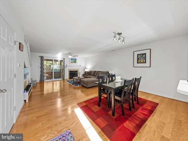 dining area with light wood finished floors, ceiling fan, and a tile fireplace