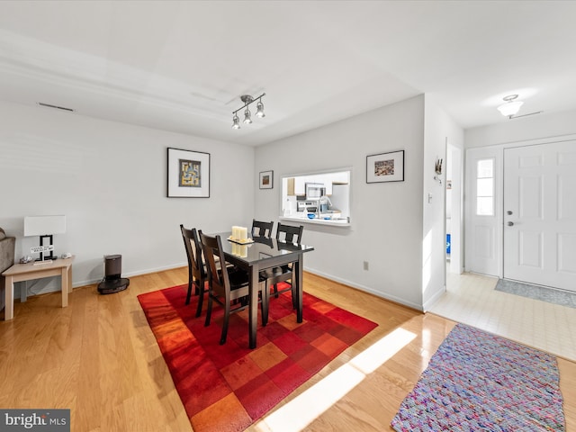 dining room featuring visible vents, baseboards, wood finished floors, and track lighting