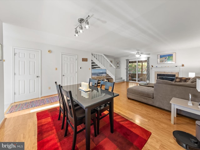 dining area featuring a ceiling fan, wood finished floors, a glass covered fireplace, stairway, and baseboards