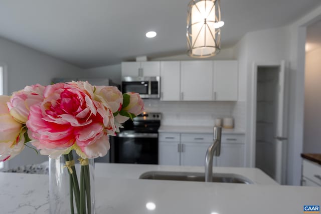 kitchen with stainless steel microwave, backsplash, electric range oven, white cabinets, and a sink