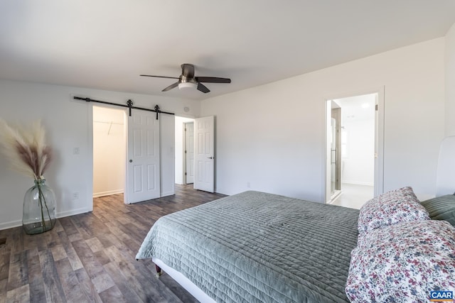 bedroom featuring a spacious closet, baseboards, a barn door, wood finished floors, and a ceiling fan