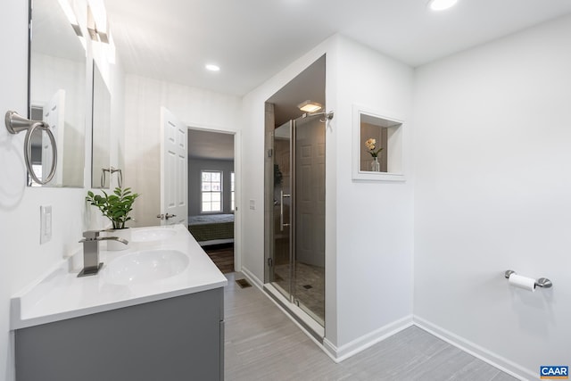 full bath with baseboards, double vanity, recessed lighting, a stall shower, and a sink