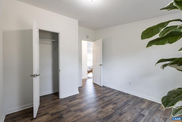 unfurnished bedroom featuring a closet, baseboards, and dark wood finished floors