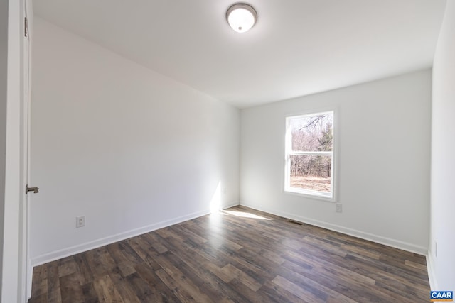 spare room featuring visible vents, baseboards, and dark wood finished floors