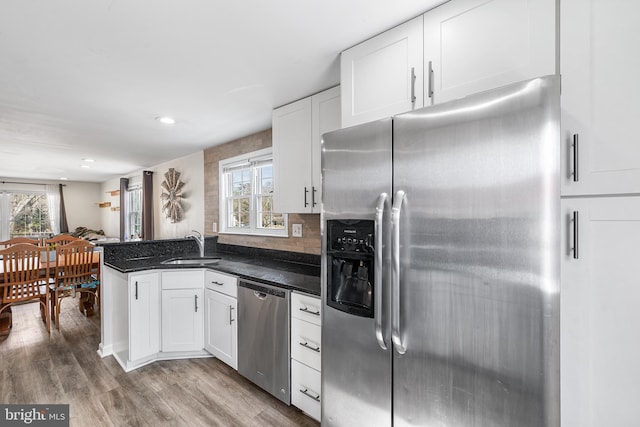 kitchen with light wood finished floors, a peninsula, stainless steel appliances, white cabinetry, and a sink