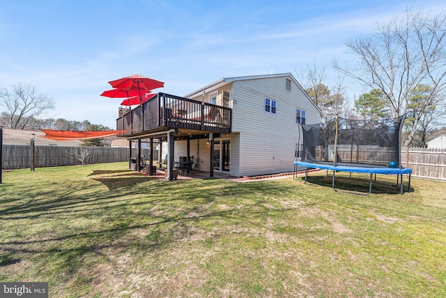 back of house with a fenced backyard, a deck, a lawn, and a trampoline