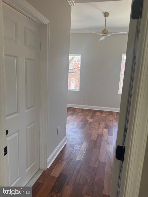 corridor with dark wood finished floors, crown molding, and baseboards