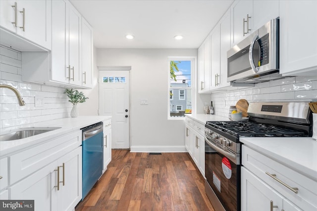 kitchen with dark wood-type flooring, a sink, stainless steel appliances, white cabinets, and baseboards