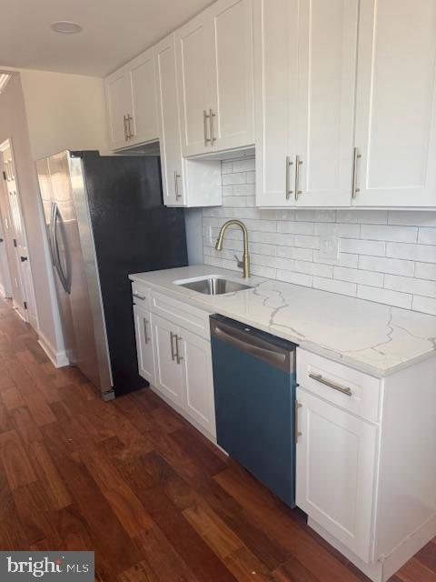 kitchen featuring light stone counters, appliances with stainless steel finishes, dark wood-style floors, white cabinets, and a sink