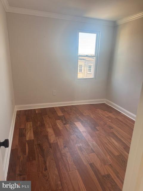unfurnished room with crown molding, baseboards, and dark wood-style flooring