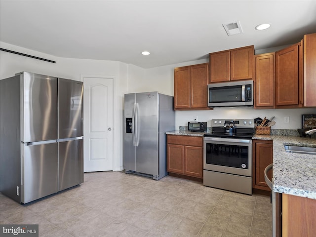 kitchen featuring brown cabinets, light stone countertops, stainless steel appliances, and a sink