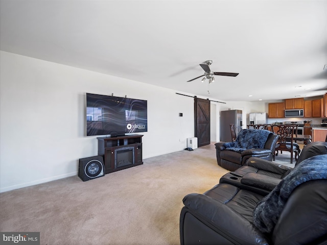 living area featuring a barn door, light carpet, baseboards, and a ceiling fan