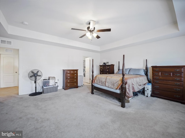 bedroom featuring a tray ceiling, carpet, visible vents, and ceiling fan