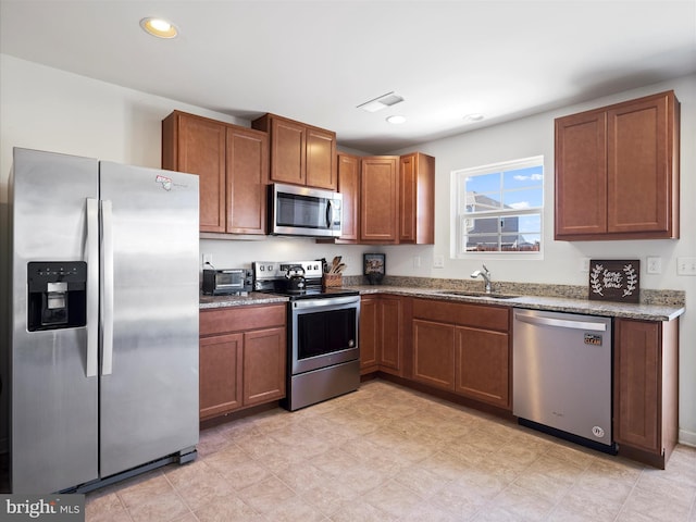 kitchen with dark stone counters, recessed lighting, a sink, appliances with stainless steel finishes, and brown cabinets