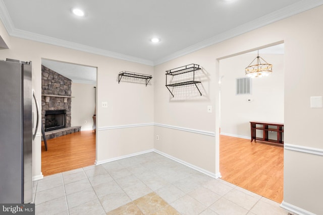 unfurnished dining area with a stone fireplace, light tile patterned flooring, and crown molding