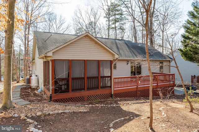 rear view of house featuring a wooden deck, a sunroom, and a shingled roof