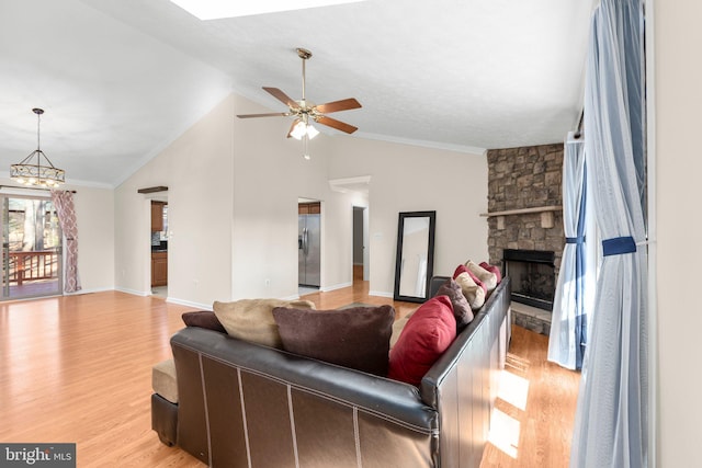 living area featuring light wood-style flooring, ceiling fan with notable chandelier, a stone fireplace, crown molding, and vaulted ceiling