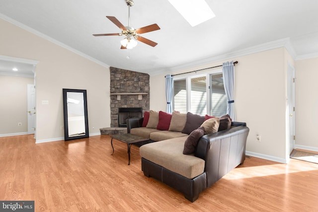 living room featuring light wood-type flooring, lofted ceiling with skylight, a fireplace, and crown molding