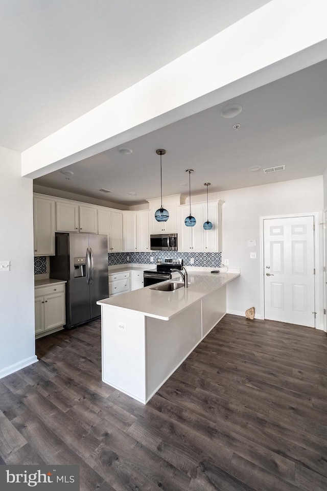 kitchen with dark wood finished floors, a peninsula, a sink, stainless steel appliances, and tasteful backsplash