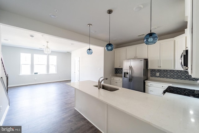 kitchen featuring dark wood finished floors, decorative backsplash, appliances with stainless steel finishes, hanging light fixtures, and a sink