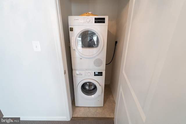 laundry area with laundry area, baseboards, stacked washer and clothes dryer, and tile patterned floors