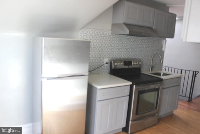 kitchen featuring stainless steel range with electric stovetop, gray cabinetry, a sink, freestanding refrigerator, and decorative backsplash