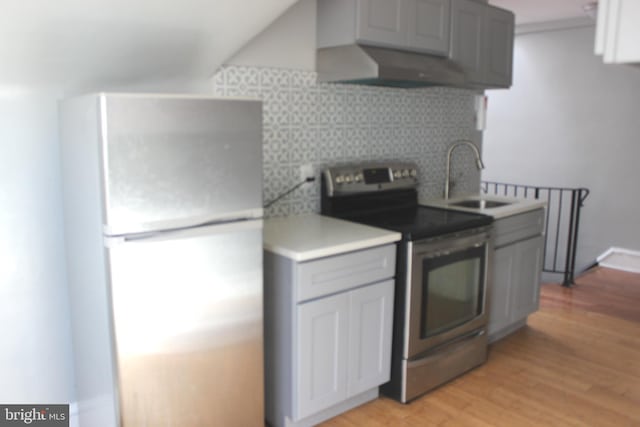 kitchen featuring stainless steel electric stove, light countertops, light wood-style flooring, freestanding refrigerator, and a sink