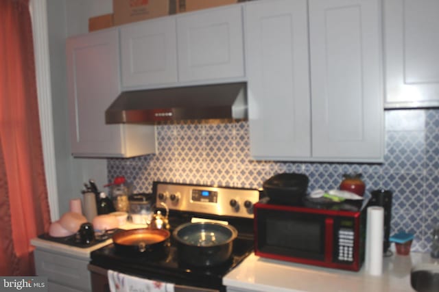 kitchen with under cabinet range hood, backsplash, stainless steel range with electric cooktop, and light countertops