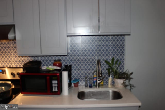 kitchen with tasteful backsplash, ventilation hood, light countertops, and a sink