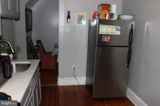 kitchen featuring dark wood-style floors, arched walkways, light countertops, and freestanding refrigerator