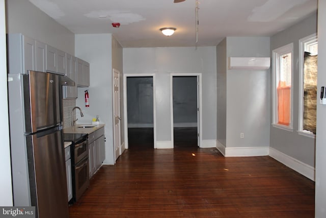 kitchen with a wall unit AC, a sink, dark wood-type flooring, appliances with stainless steel finishes, and a wealth of natural light