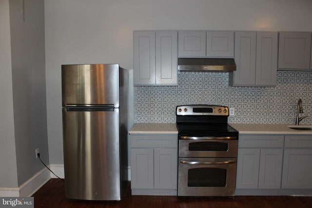 kitchen featuring gray cabinetry, under cabinet range hood, a sink, stainless steel appliances, and light countertops